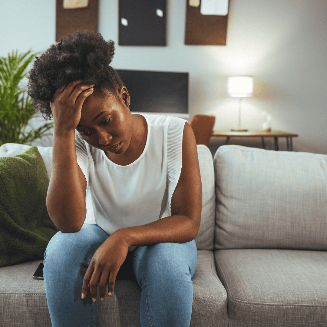 An image from Canva of a sad young black woman sitting on the couch.